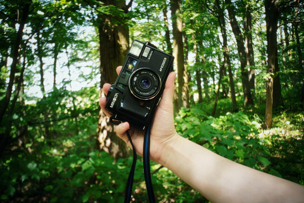 Closeup of a Minolta hi-Matic Af2-M held by a persons hand in a forest.